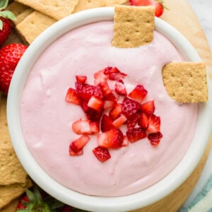 Two graham cracker pieces sit in a bowl of strawberry cream cheese dip.