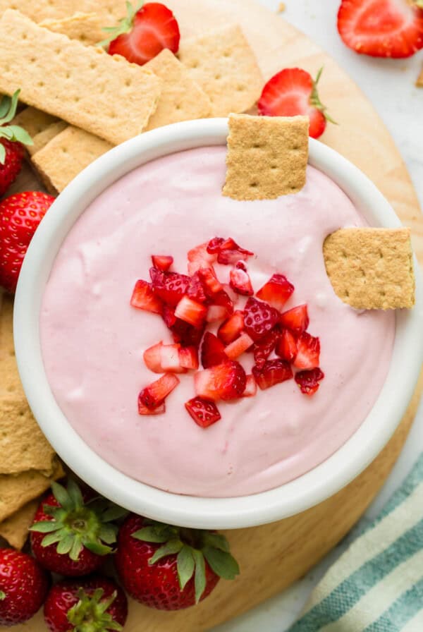 Two graham cracker pieces sit in a bowl of strawberry cream cheese dip.