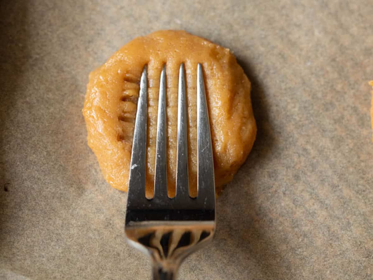 A fork pressing into a peanut butter cookie to get it crisscross marks.