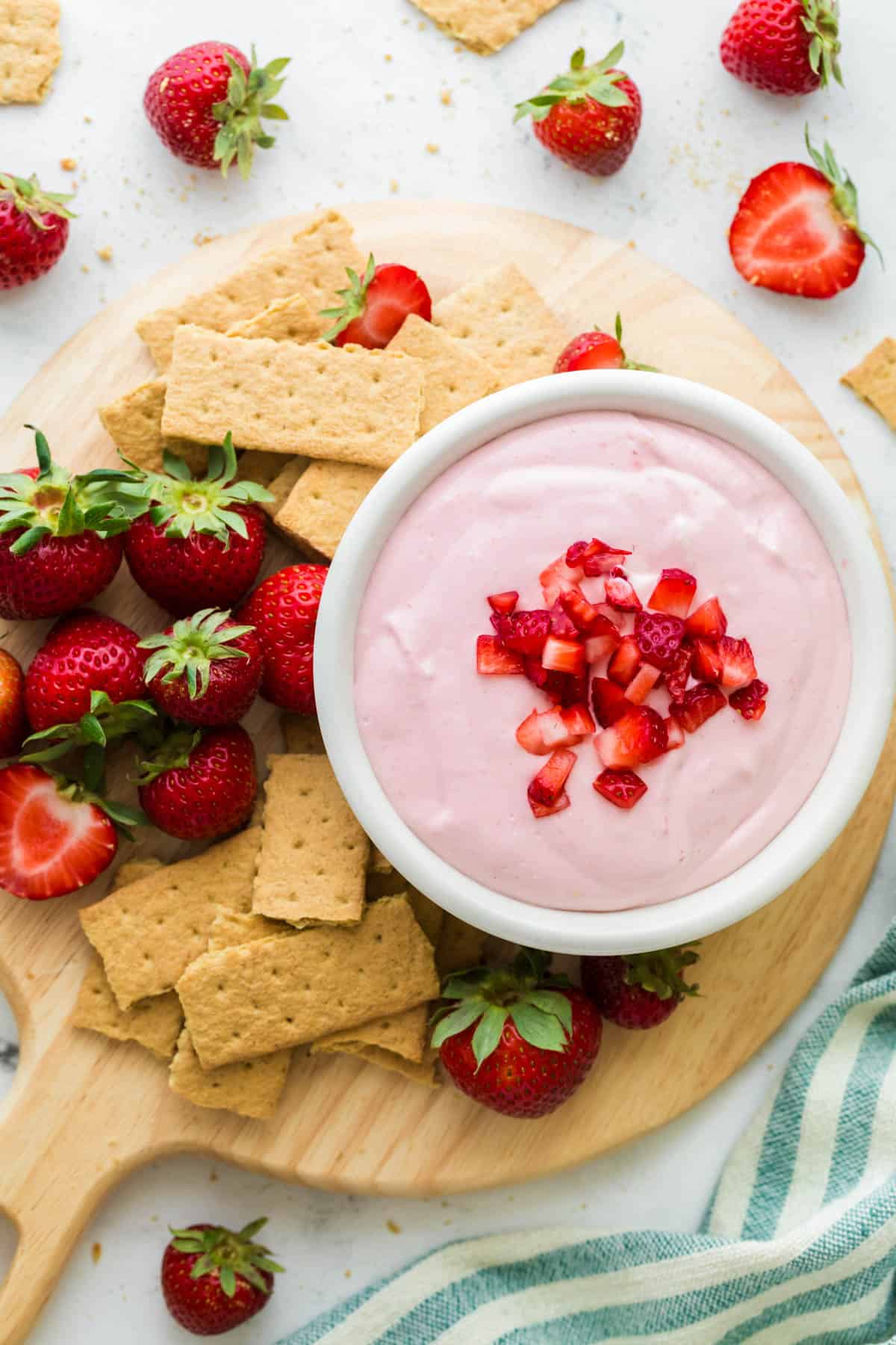 Strawberry Cheesecake Dip in a white bowl on a wooden cutting board served with graham crackers and fresh strawberries.