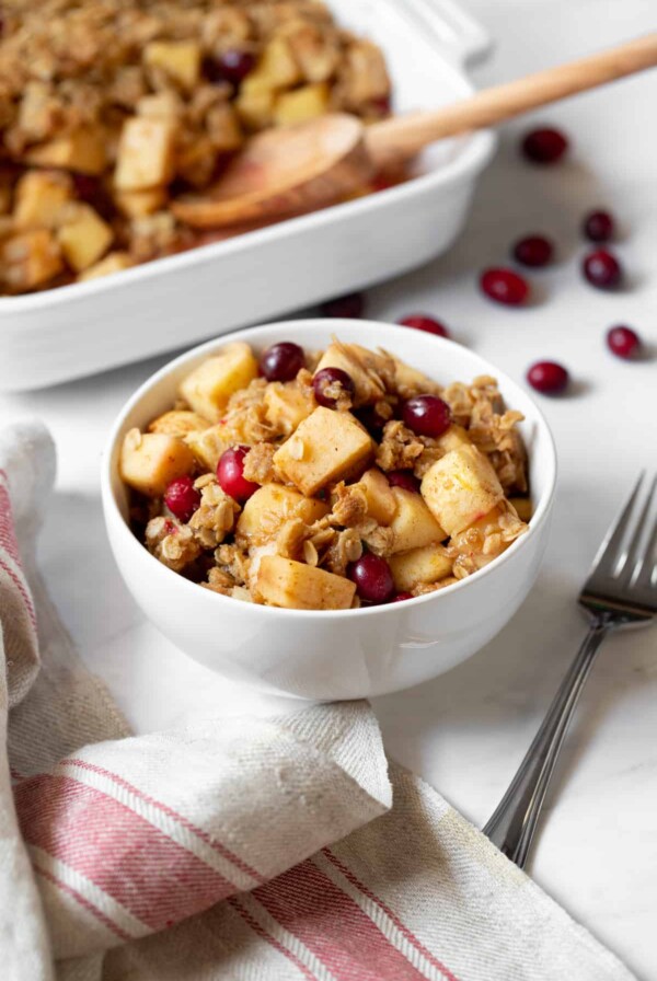 a bowl of apple, pear and cranberry crisp sitting on a table with a fork on the side