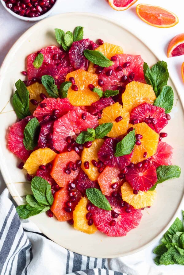 a white plate with citrus salad on top garnished with pomegranate seeds and fresh mint