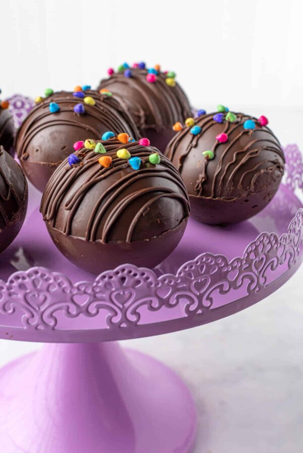 hot chocolate balls filled with hot cocoa sitting on a purple cake stand