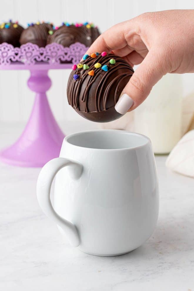 dropping one hot chocolate ball into a mug before filling with hot milk