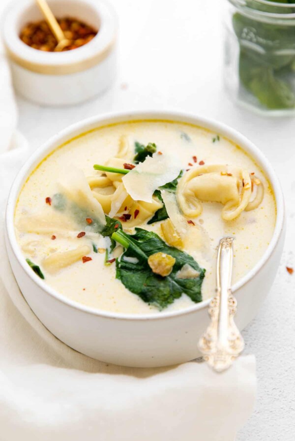 a bowl of tortellini soup sitting on a white table