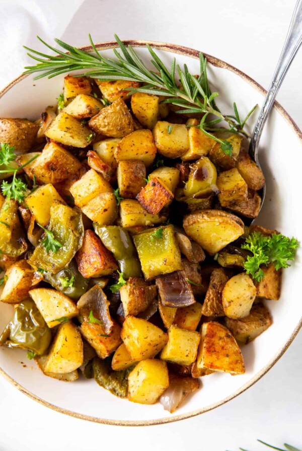 baked breakfast potatoes in a white bowl with a large spoon