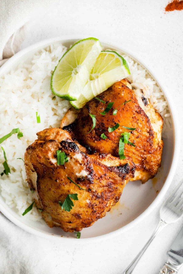 two chicken thighs on a plate with a side of rice and lime slices