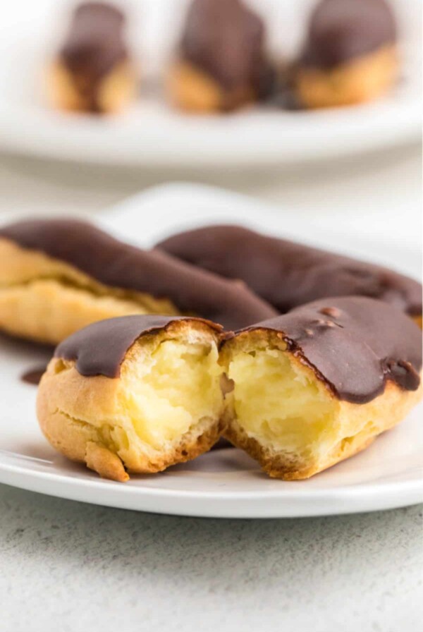 Three eclairs on a plate, one cut in half to show the vanilla cream center.