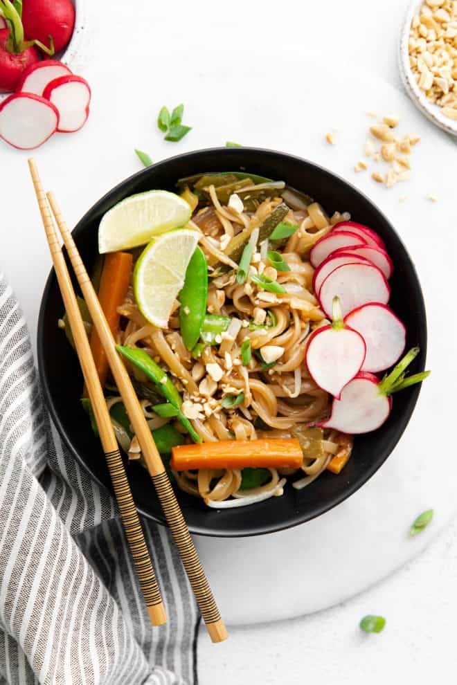 A bowl of vegetarian pad thai garnished with radish and lime, and a pair of chopsticks laying across the bowl. 