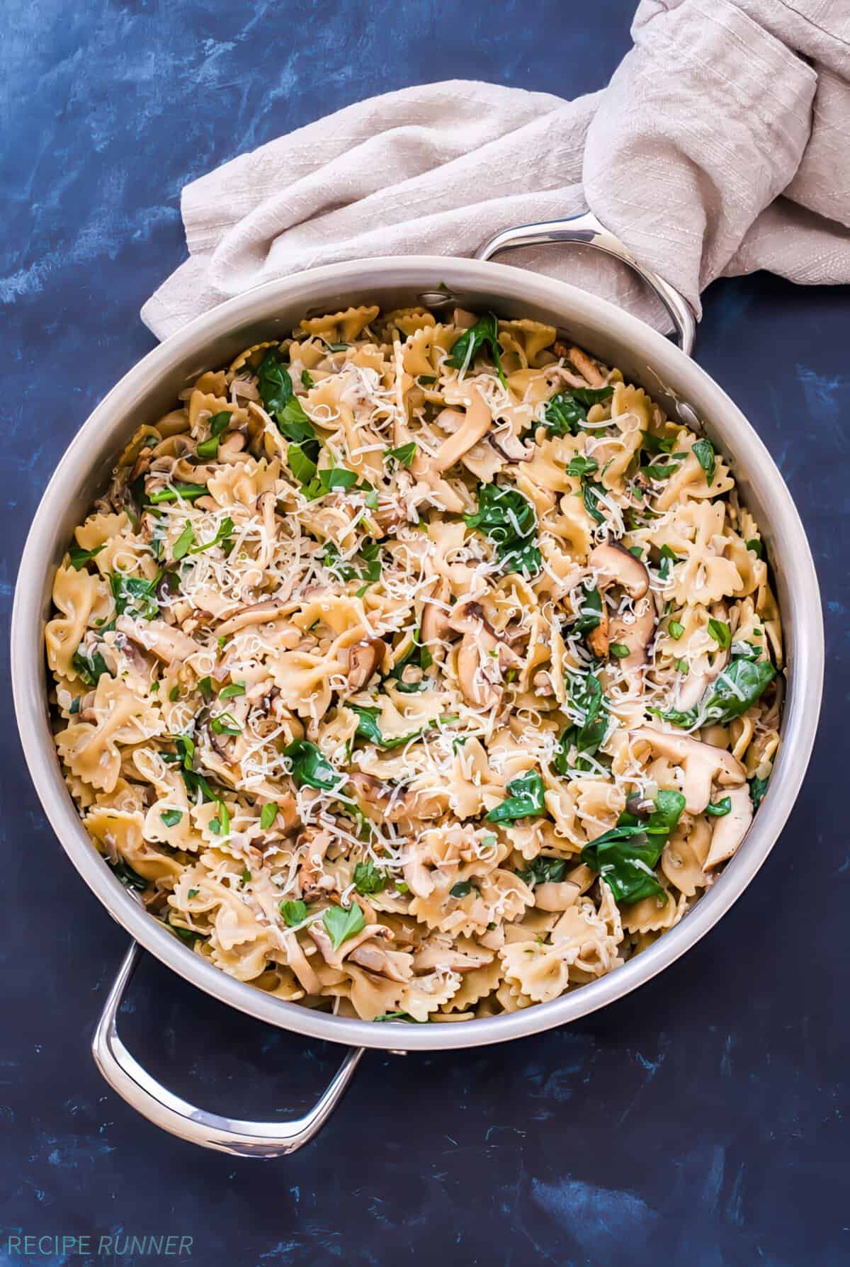 Cooked spinach mushroom pasta in a skillet with Parmesan cheese sprinkled on top