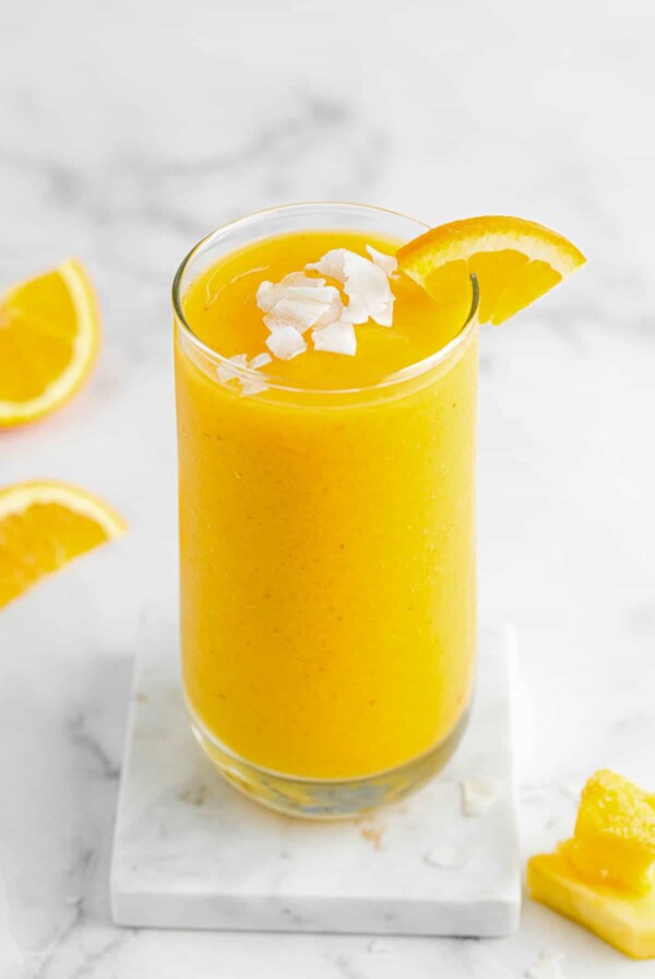 a glass of citrus smoothie with coconut flakes and sliced orange on top