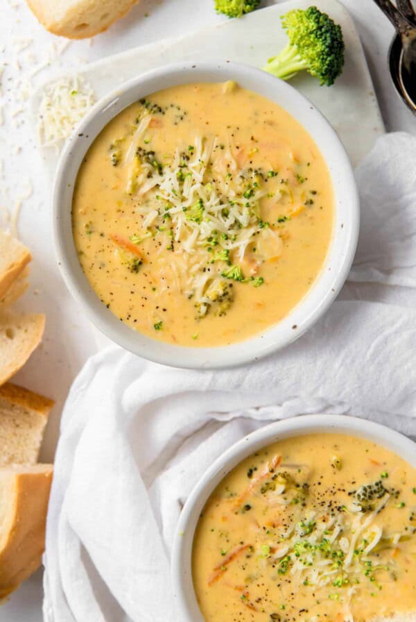 two bowls filled with broccoli cheddar soup with sprinkle of cheese on top