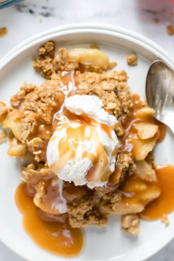 Homemade apple crisp on a white plate with a scoop of vanilla ice cream and a drizzle of caramel sauce.