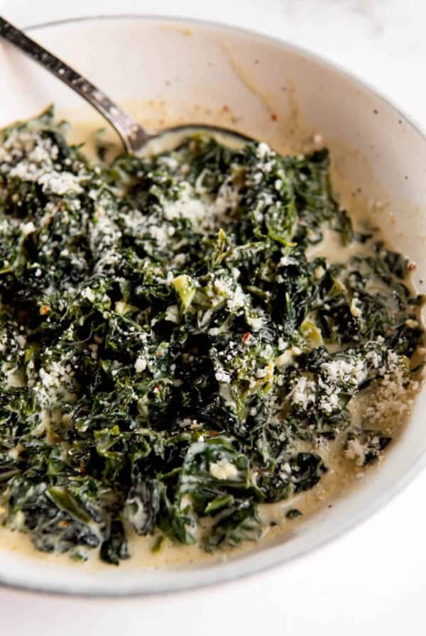 creamed kale with parmesan cheese one top in a bowl with a serving spoon