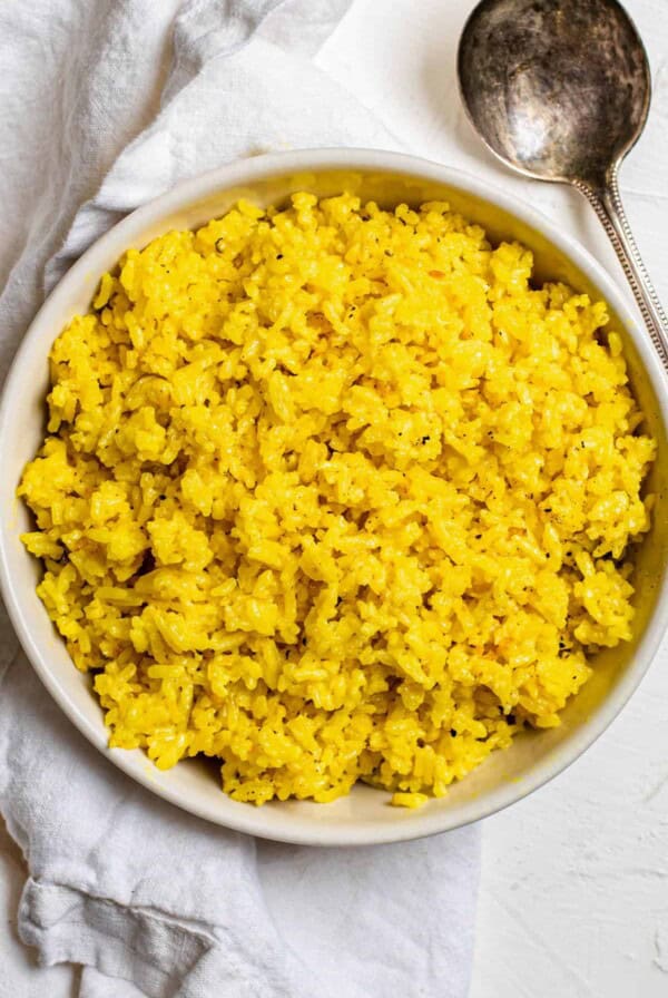 A large white bowl filled with cooked turmeric coconut rice.