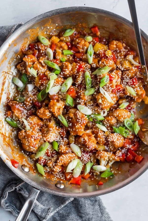 sweet and sour cauliflower with sliced green onions and sesame seeds in a skillet