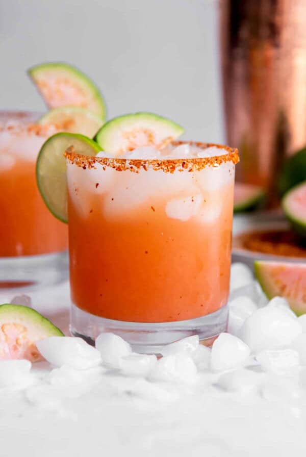 One guava margarita sitting on a white countertop with slices of lime as garnish.