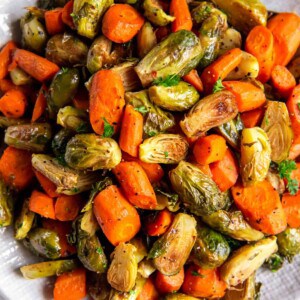 A large white bowl filled with roasted brussels sprouts and carrots sitting on a white countertop.