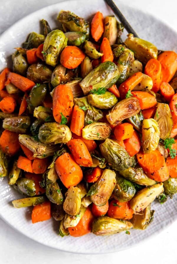 A large white bowl filled with roasted brussels sprouts and carrots sitting on a white countertop.