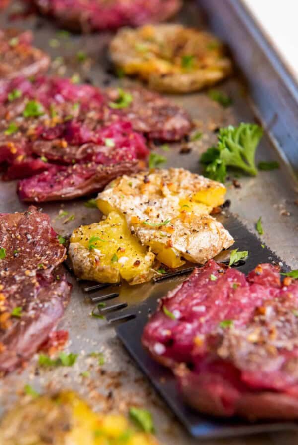 A spatula picks up smashed fingerling potatoes off of a baking sheet after baking in the oven.