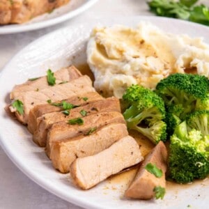 A cooked pork chop sliced into many pieces and served on a plate with cooked broccoli and mashed potatoes.