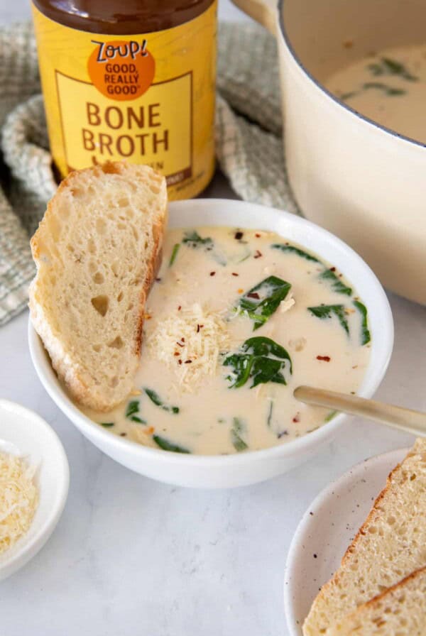 A bowl of chicken florentine soup sitting on a white countertop with a jar of zoup chicken bone broth in the background.