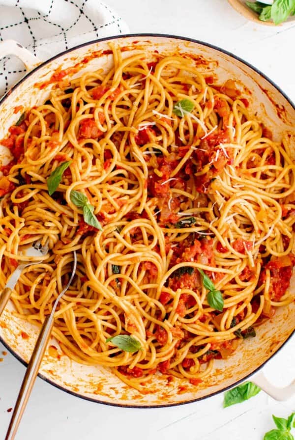 A pan filled with cooked spaghetti arrabbiata and garnished with chopped basil.