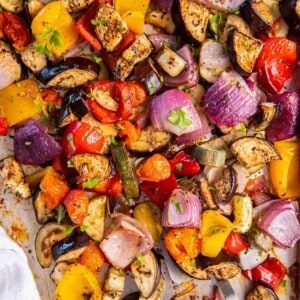 Mediterranean Roasted Vegetables on a sheet pan ready for serving. A spoon scoops up some of the vegetables.