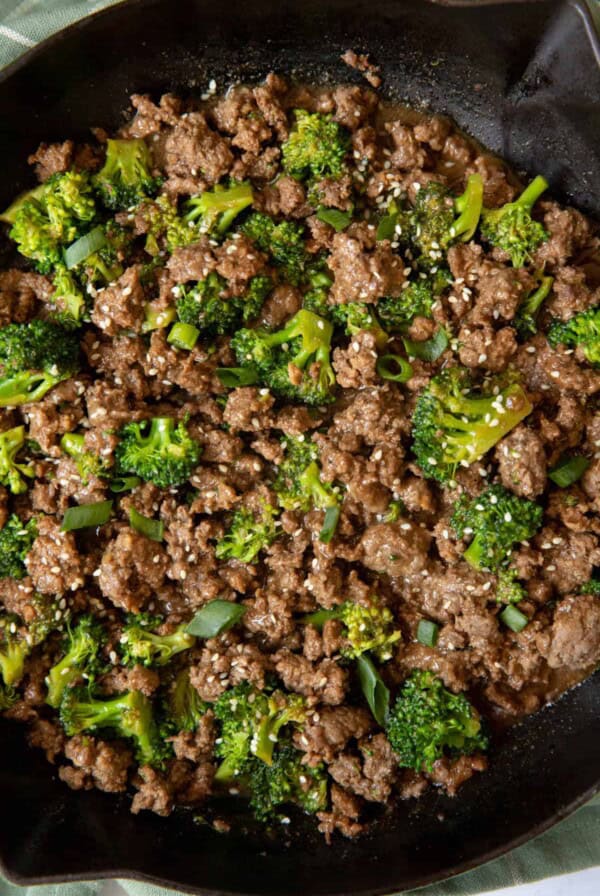 Cooked ground beef and broccoli in a skillet with sesame seeds and sliced green onions garnished on top.