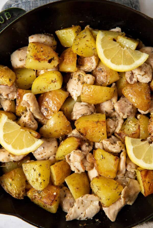 Cooked Italian chicken and potatoes in a skillet ready for serving. Lemon wedges are garnished on top.