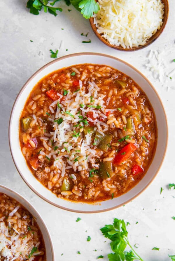 A bowl of instant pot stuffed pepper soup sitting on a white countertop with a bowl of fresh parmesan cheese on the side.