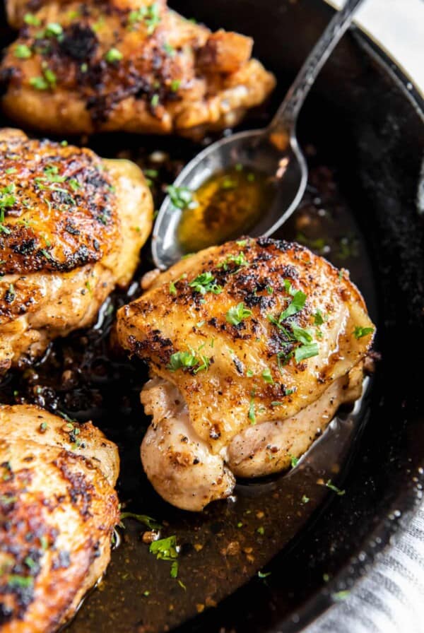 A spoon with melted butter sits in the cast iron skillet next to the cooked cast iron chicken thighs.