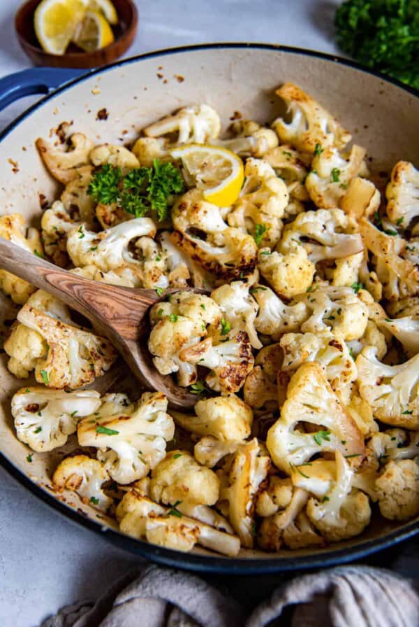 Sauteed cauliflower in a blue enameled skillet. A wooden spoon is starting to take a scoop of the cooked cauliflower.