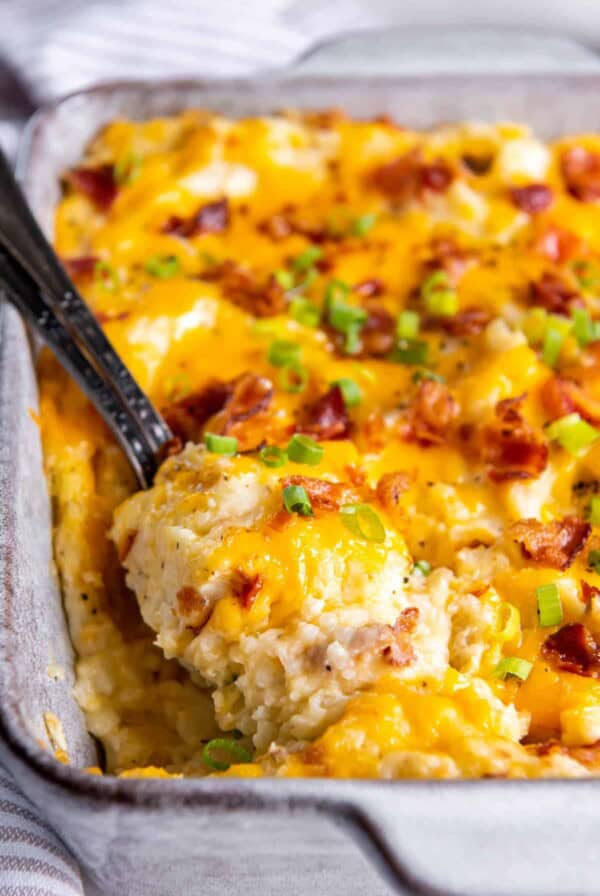 A casserole dish filled with twice baked mashed potatoes. A spoon is sitting in the dish ready to serve the mashed potatoes.