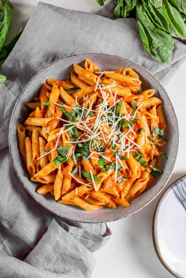 A bowl filled with tomato basil pasta with fresh Parmesan and basil sprinkled on top.