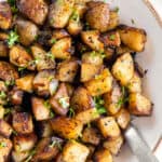 Crispy pan fried potatoes and onions in a large white serving bowl with a spoon for serving.