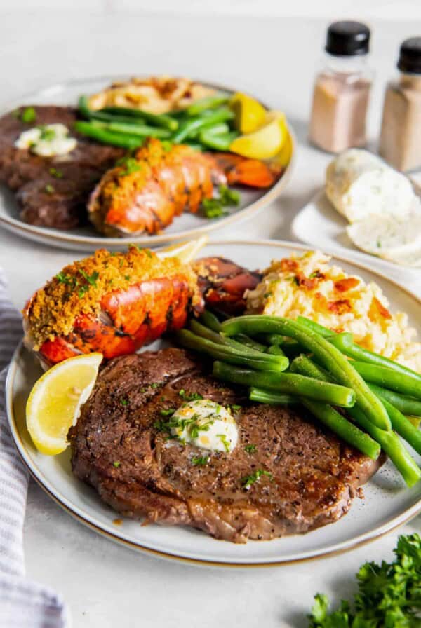 Steak and lobster plated on a plate with mashed potatoes and green beans.