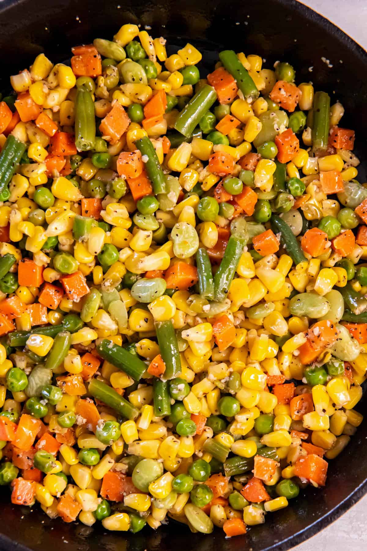 A cast iron skillet is filled with cooked buttered mixed vegetables.