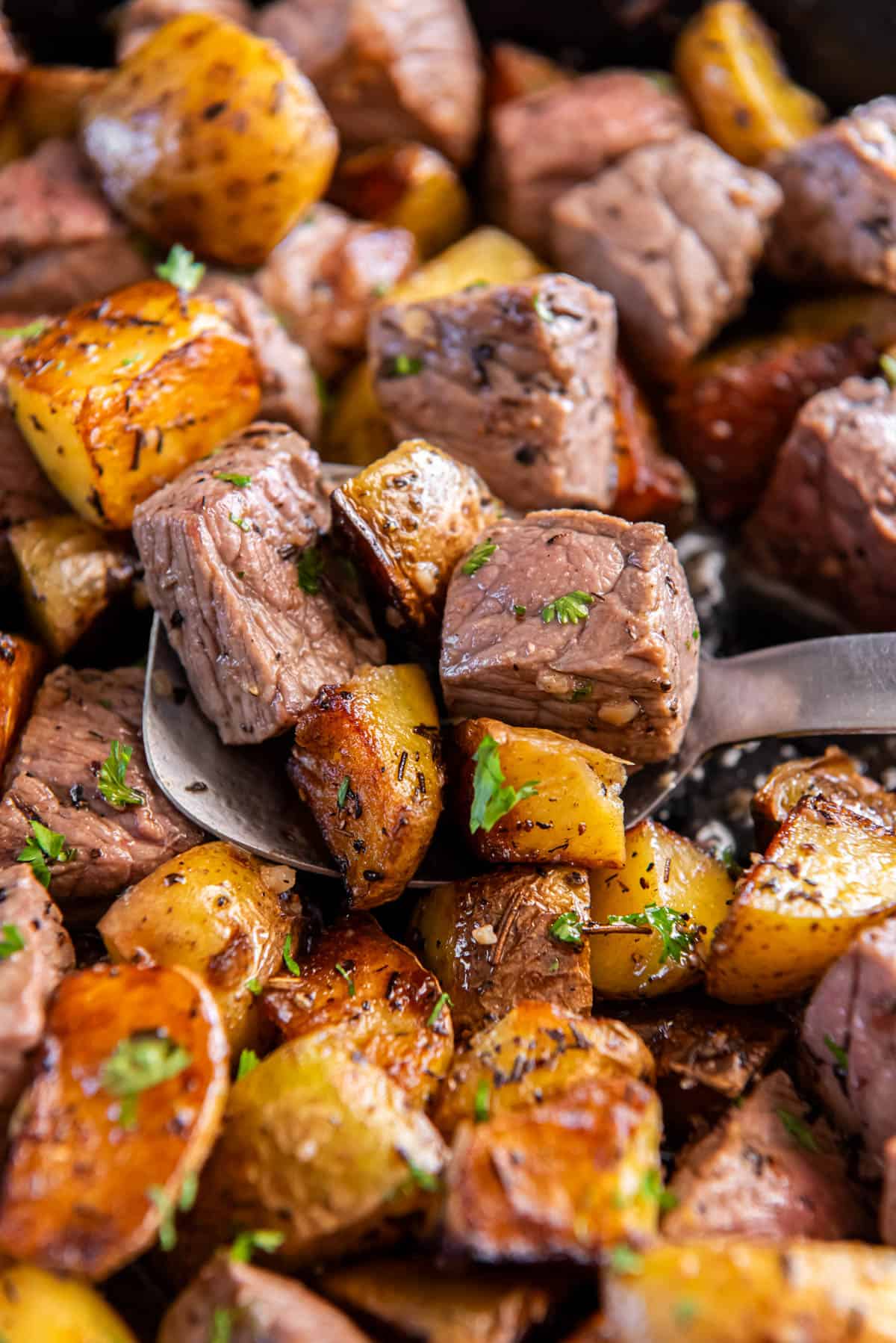 A serving spoon scooping out the cooked steak and potatoes for serving.