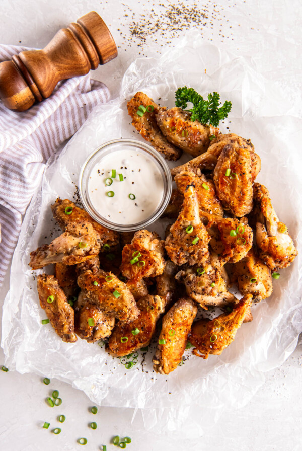 Salt and pepper chicken wings sitting on a white plate with a bowl of dipping sauce sitting on the side for serving.