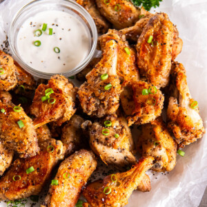 Salt and pepper chicken wings on a white plate with dipping sauce.