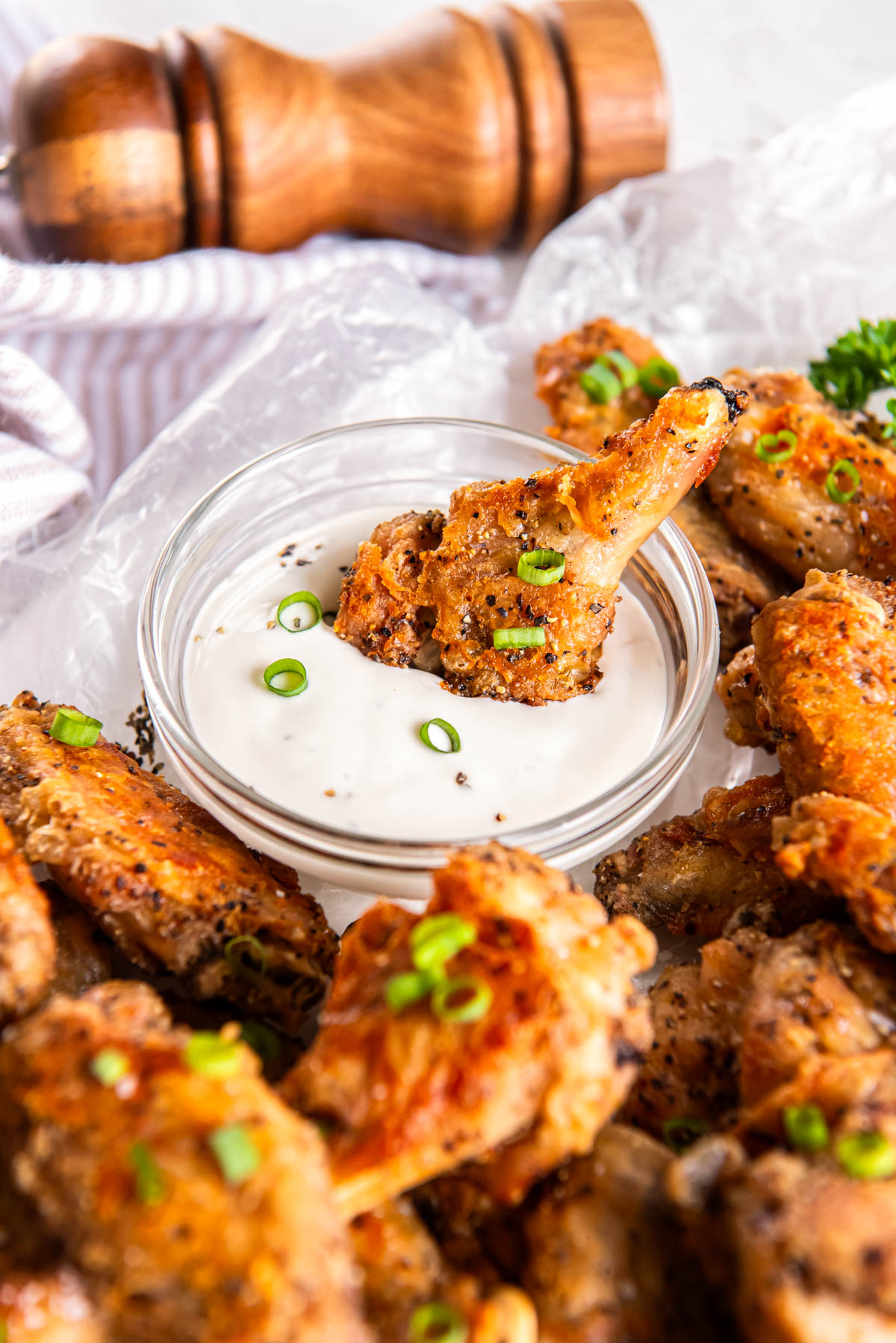 One chicken wing dipped in ranch dressing before serving. The remaining chicken wings sit on a plate on the side for serving.