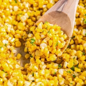 A spoon scoops out sautéed corn from a skillet for serving.