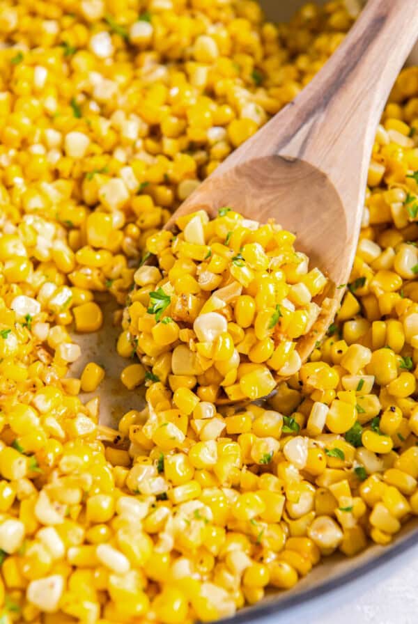 A spoon scoops out sautéed corn from a skillet for serving.