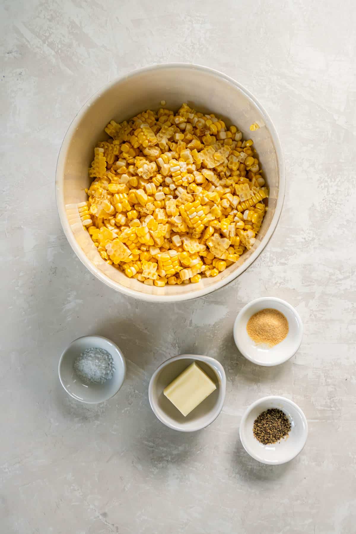 All of the ingredients for sauteed corn in prep bowls on a white countertop. 