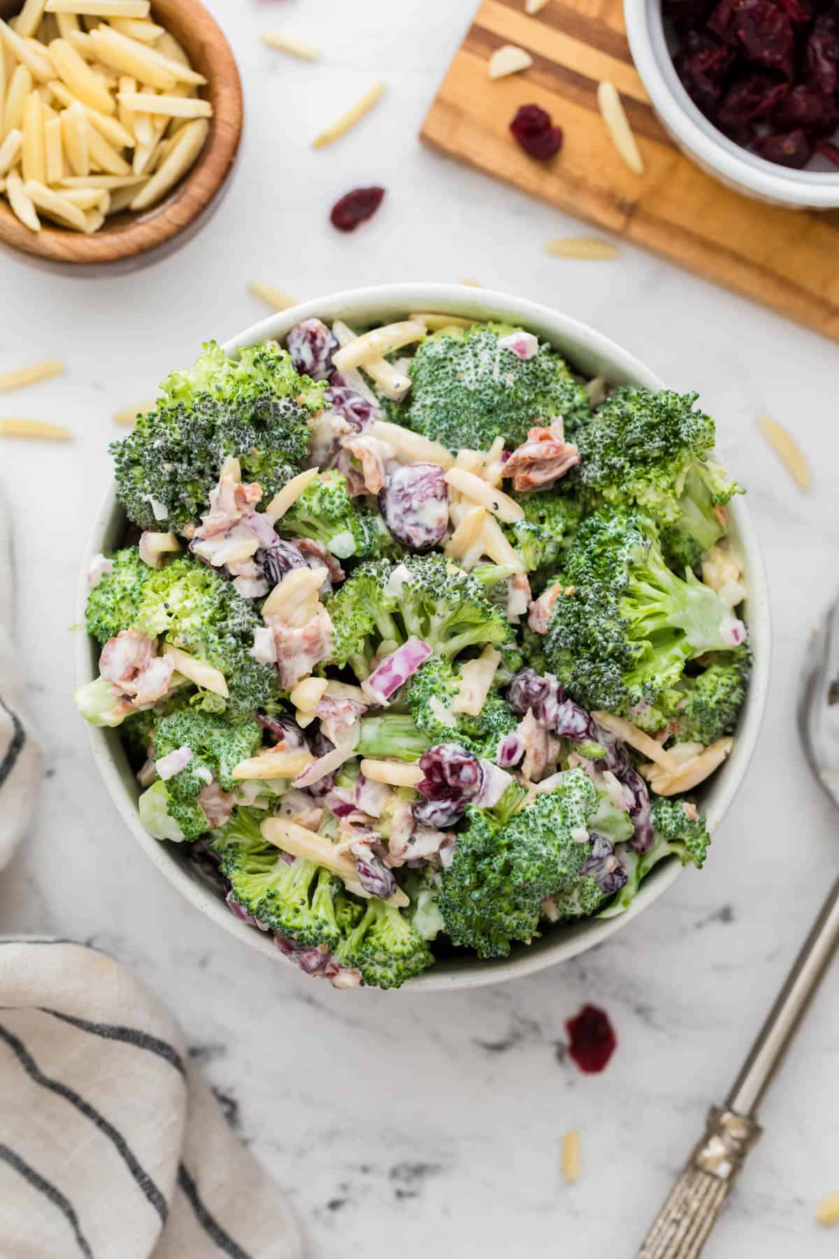 A large bowl filled with crunchy broccoli salad sits on a white countertop ready for serving. 