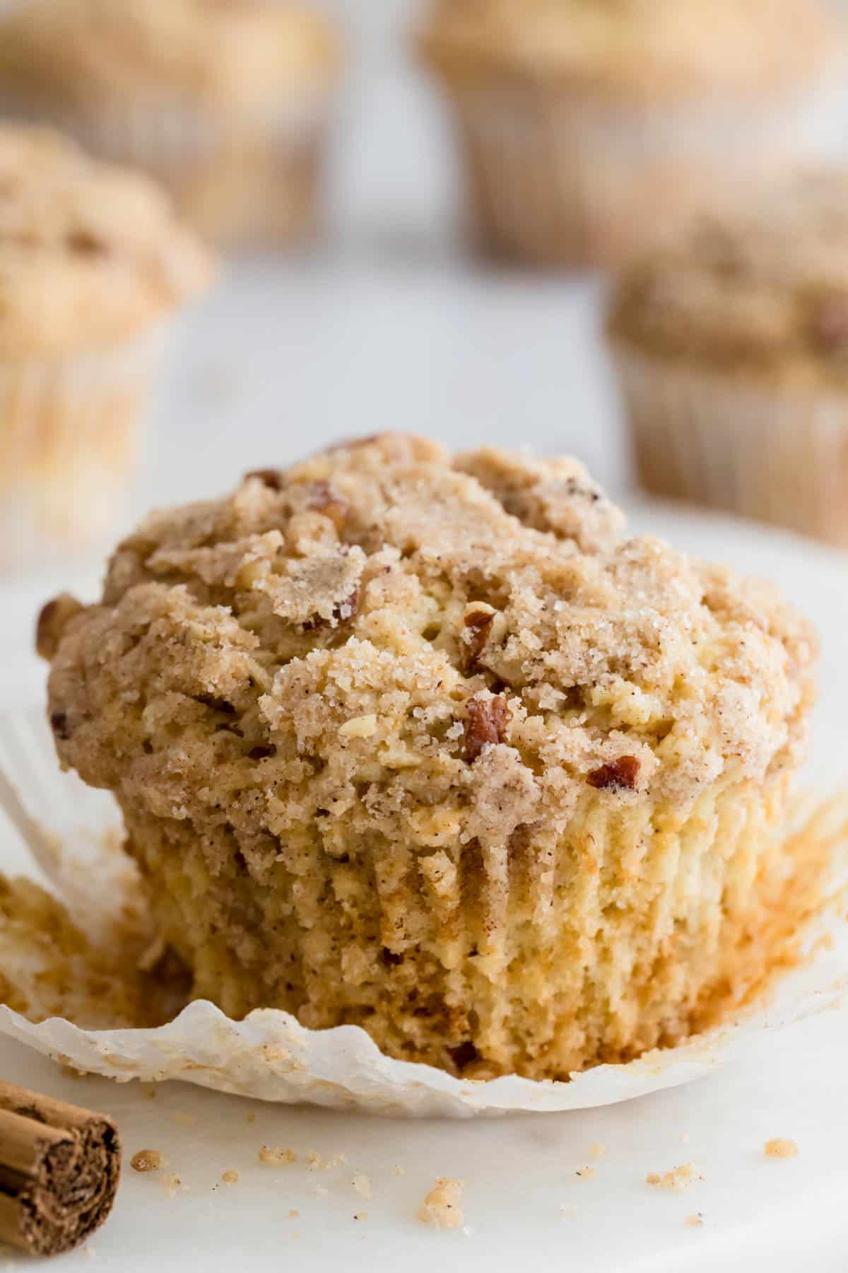 One coffee cake muffin sits on a paper baking liner on a countertop ready to be eaten.