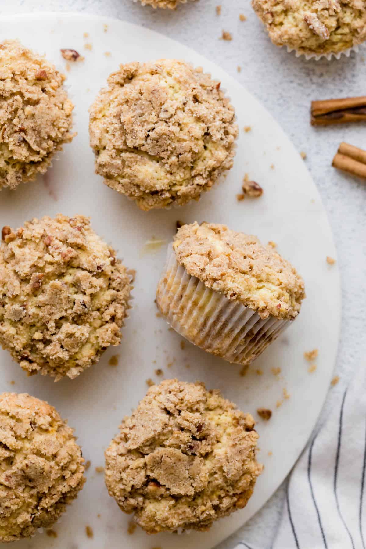 Six coffee cake muffins sit on a white serving platter with crumbs on the side. 