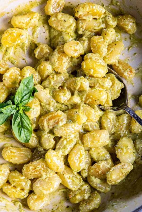 A spoon scoops out creamy pesto gnocchi from the pan for serving.