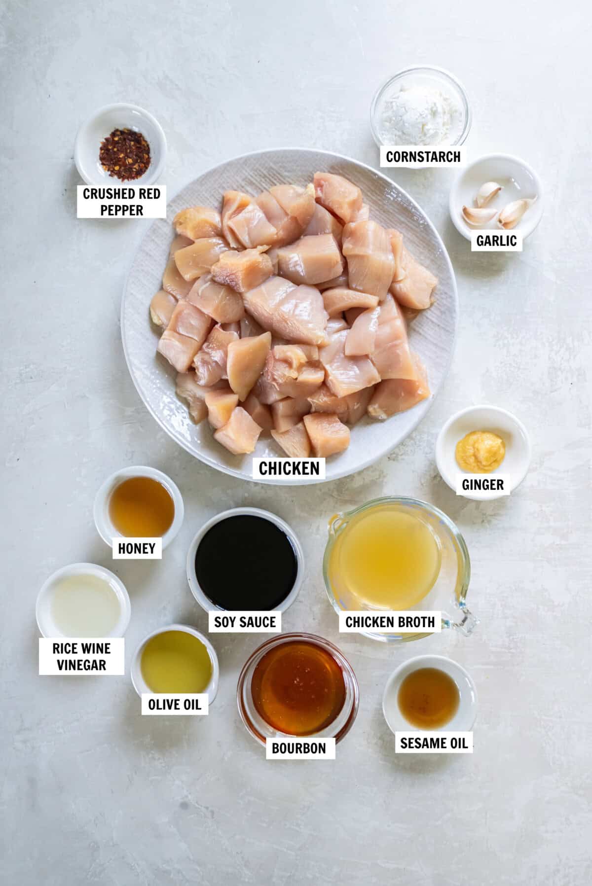 All of the ingredients for honey bourbon chicken in bowls on a white countertop. 